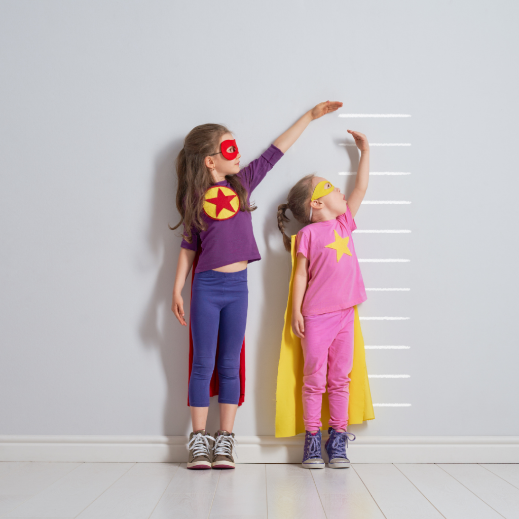 Two children compare their heights to one another while dressed as superheros.