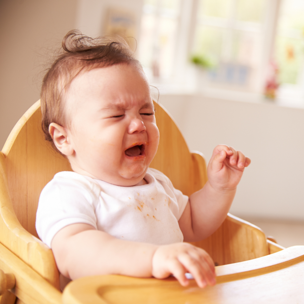 A baby sitting in a high chair, crying and visibly upset.