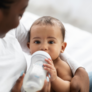 Baby laying down with mother drinking a bottle of milk.