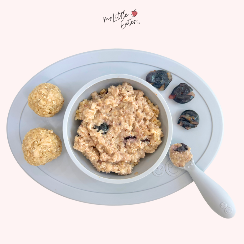 Baby-led weaning recipe containing whole milk, blueberries, and quinoa on a light pink background; plated in an ezpz bowl.