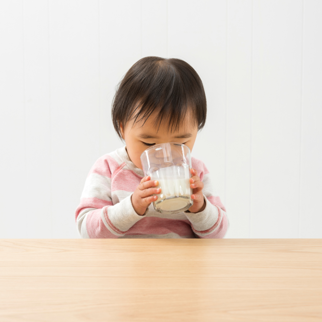 Toddler sitting at the table drinking a glass of milk.