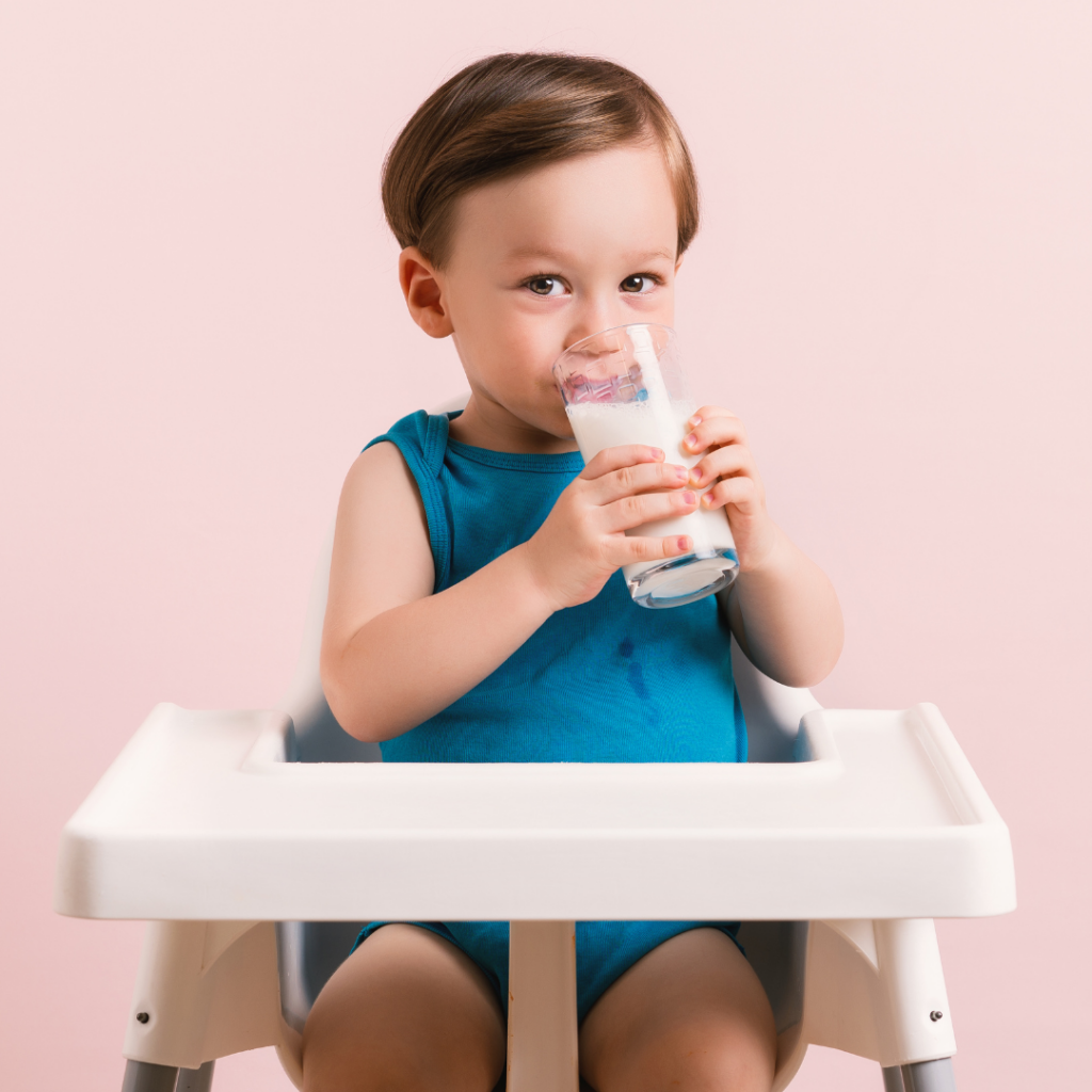 Toddler sitting in a high chair drinking a tall glass of non-dairy milk.