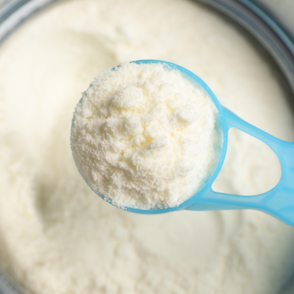 Overhead view of a container of powdered formula and a blue scoop overfilled with powdered formula.