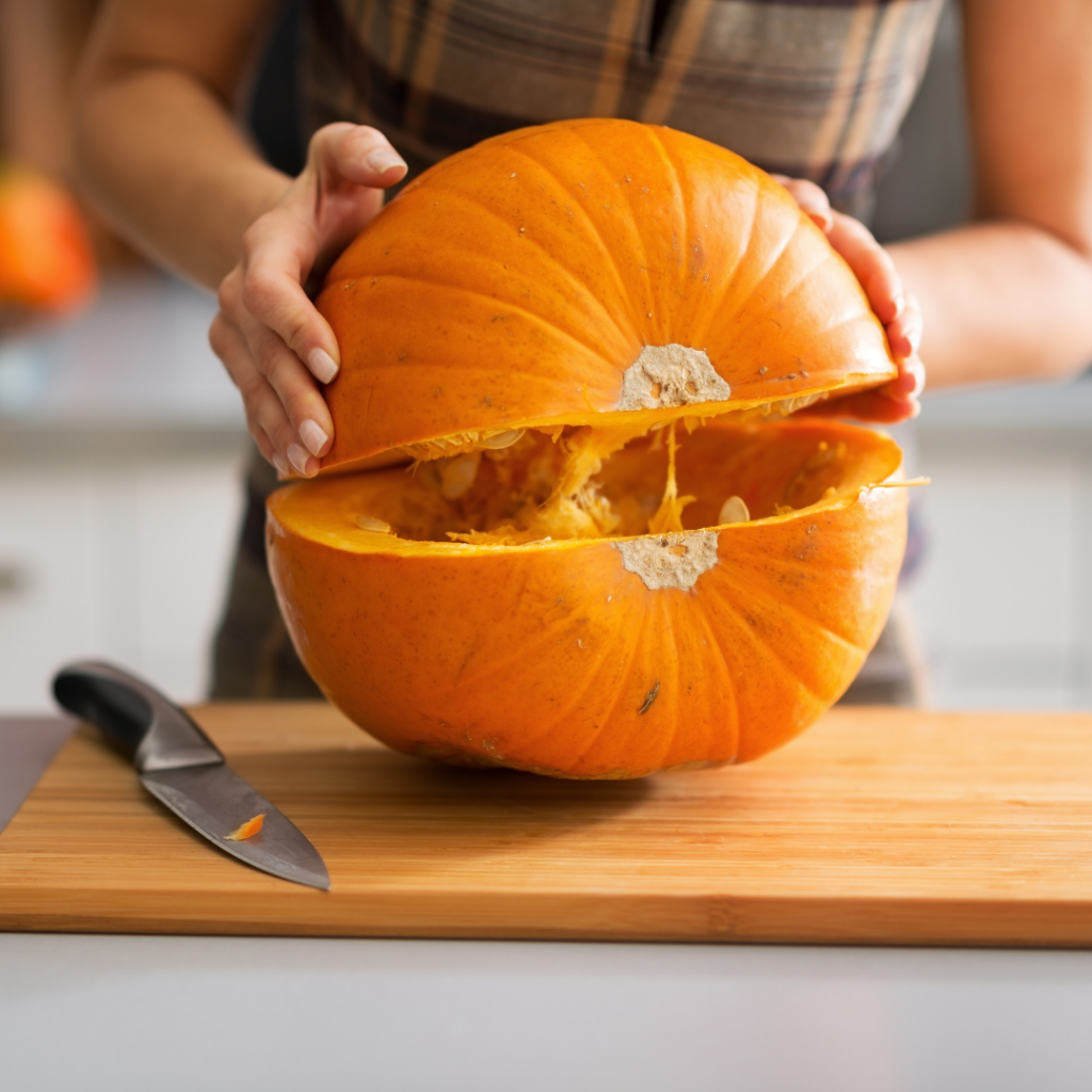 A pumpkin on a cutting board being cut in half and pulled apart.