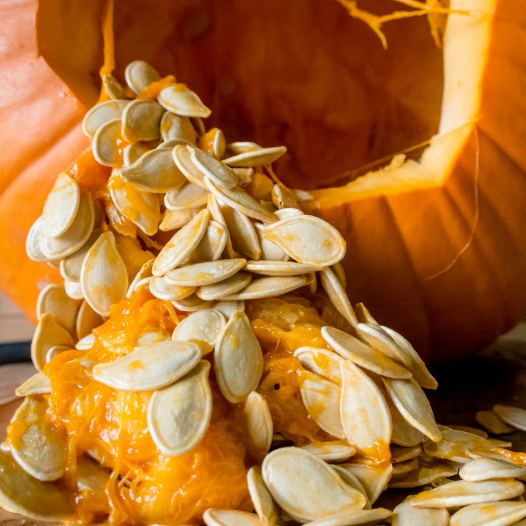 A pumpkin cut open at the top, tilted to the side, with seeds and flesh falling out of it.