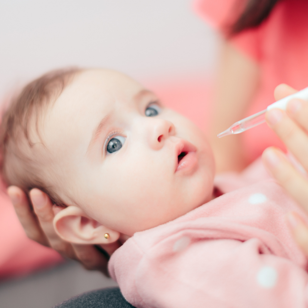 A parent provides a vitamin supplement to their baby through a dropper.