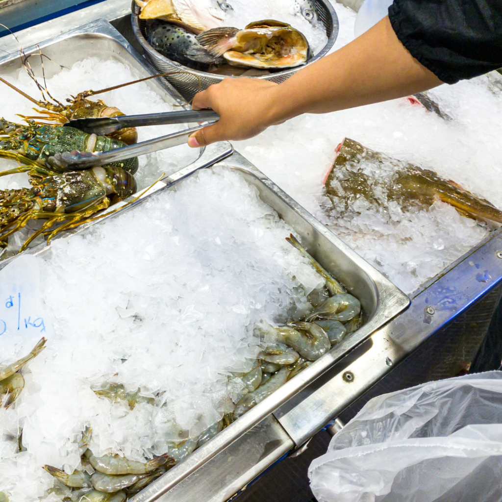 Picking up seafood with tongs that is stored on ice at a fish market.