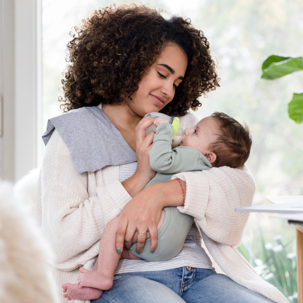 A mother cradles her baby while feeding them their bottle.