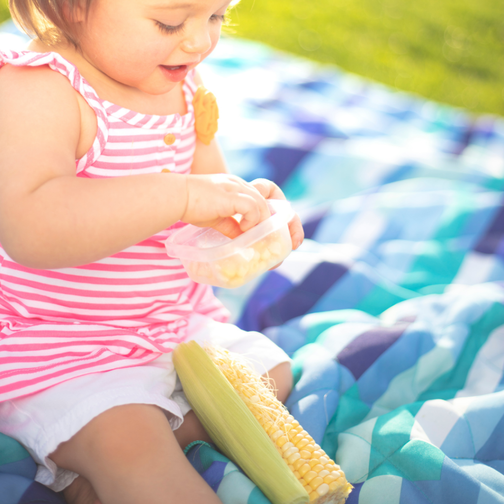 Toddler developing healthy eating habits through snacking on different foods in their whole form, including corn on the cob.