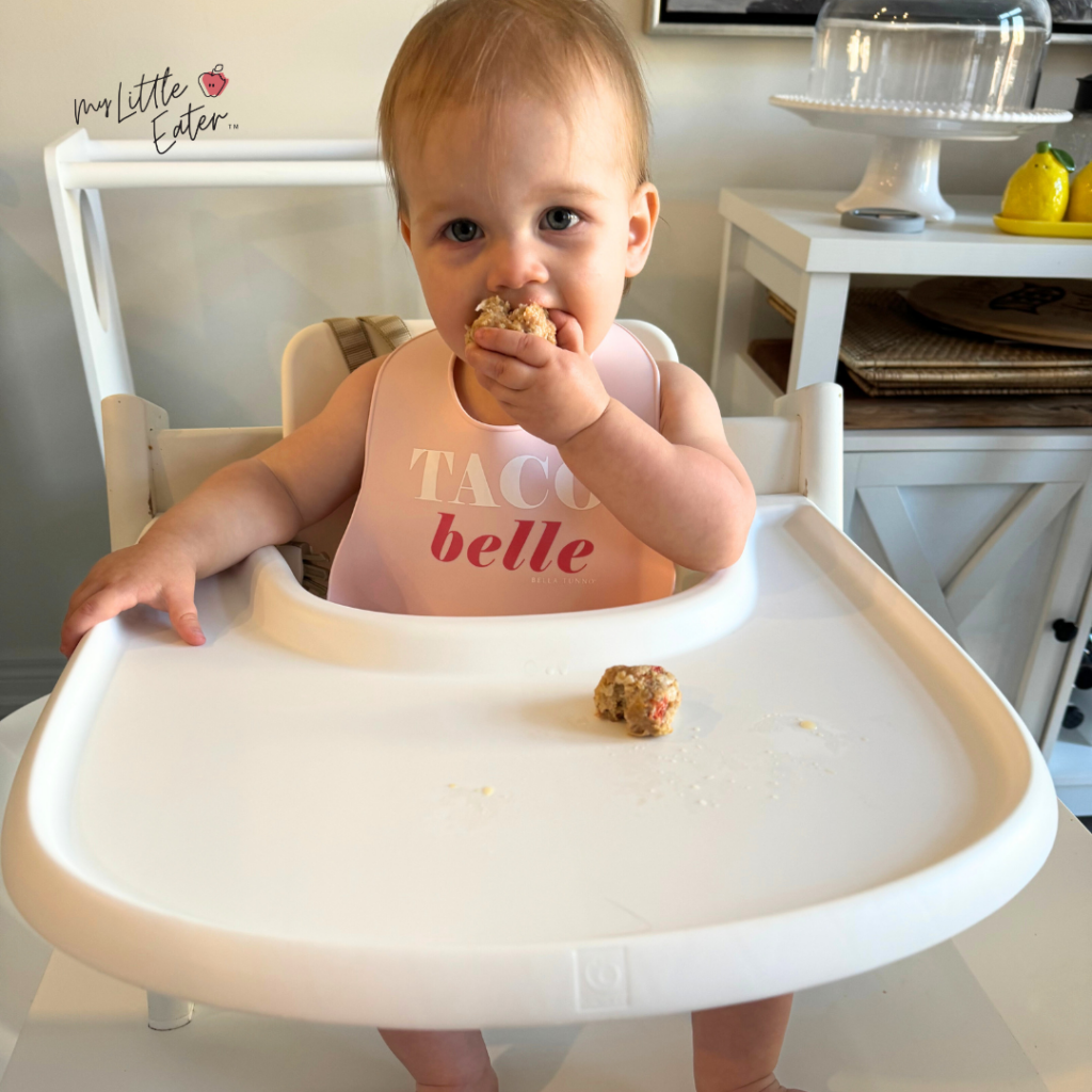 A baby sits in her high chair eating baby meatballs perfectly fine with no issues.