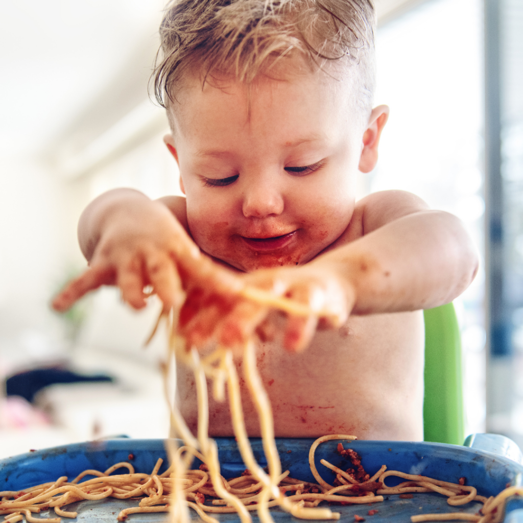 Food play with cooked pasta, baby digs into a plate of spaghetti.