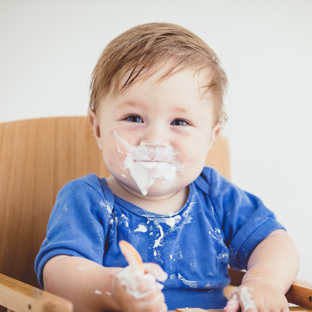 Baby in a high chair doing edible sensory play with yogurt.