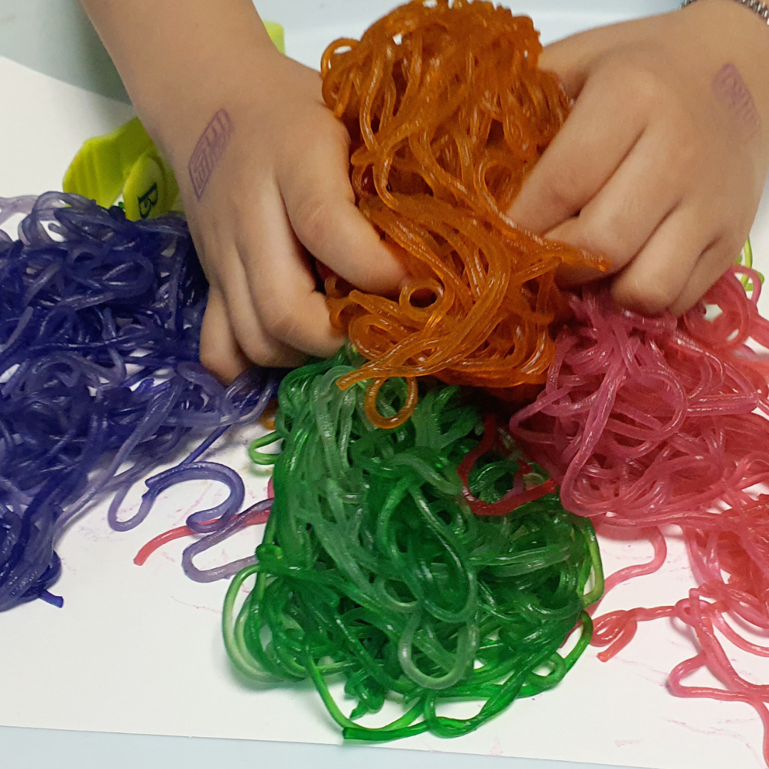 Cooked noodles dyed with food coloring for older kids, toddlers, and babies to explore through various edible sensory play ideas.