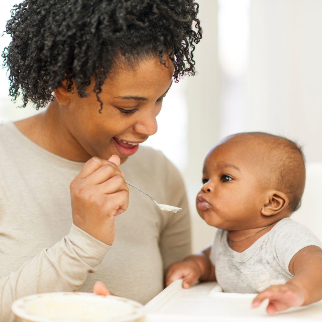 A mother feeding their baby some baby food on a spoon.