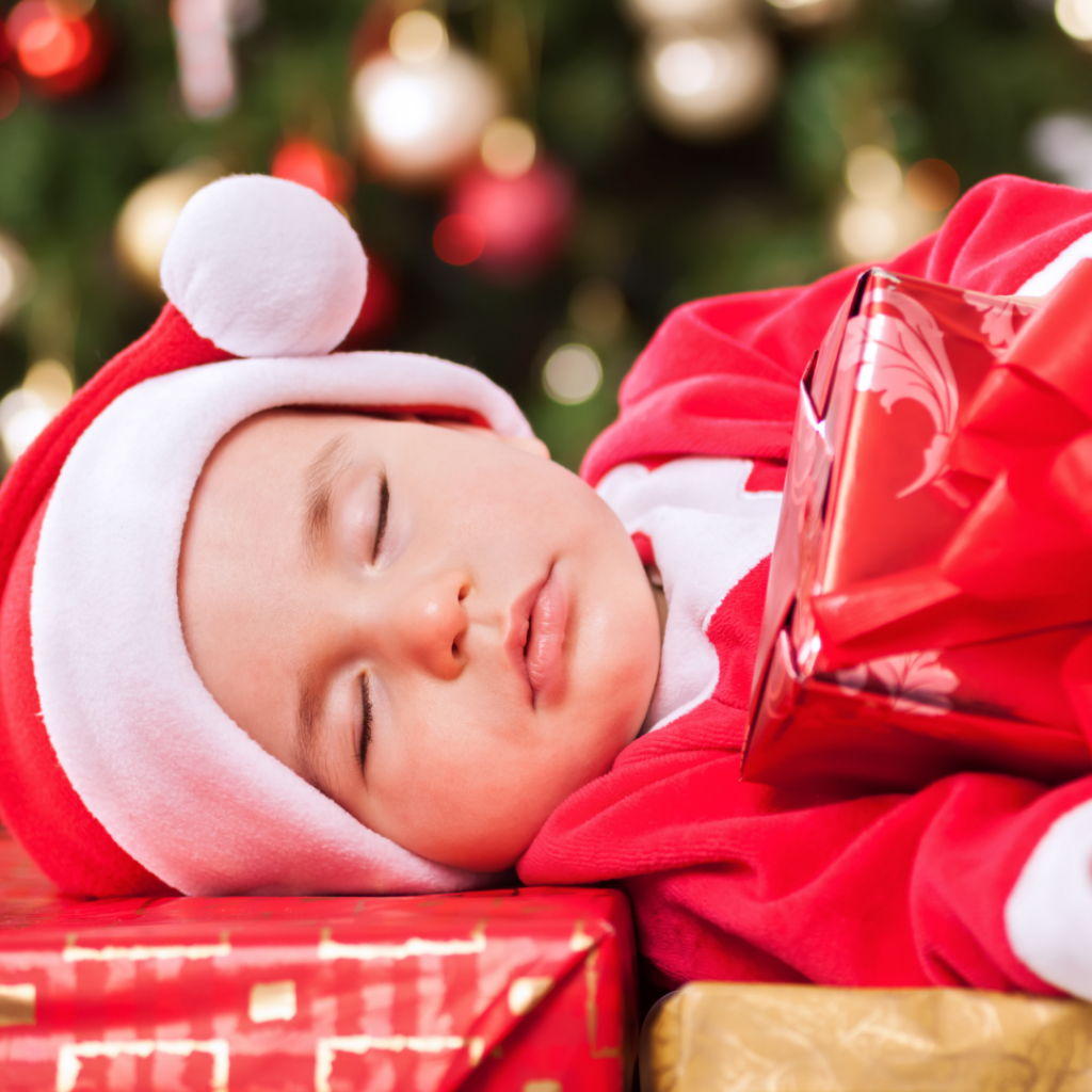 Baby sleeping under a Christmas tree.