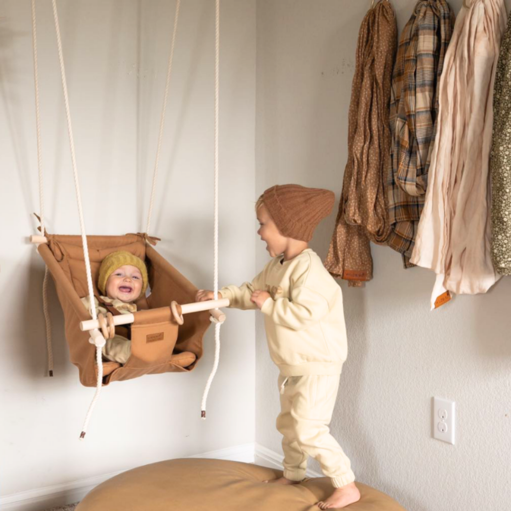 Toddler pushing baby in an indoor swing by Sweet Swinging.