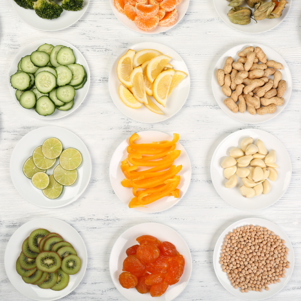 Various foods cut and served on white plates, including kiwis, lime, pepper, cucumbers, tangerines, peanuts, and apricots.