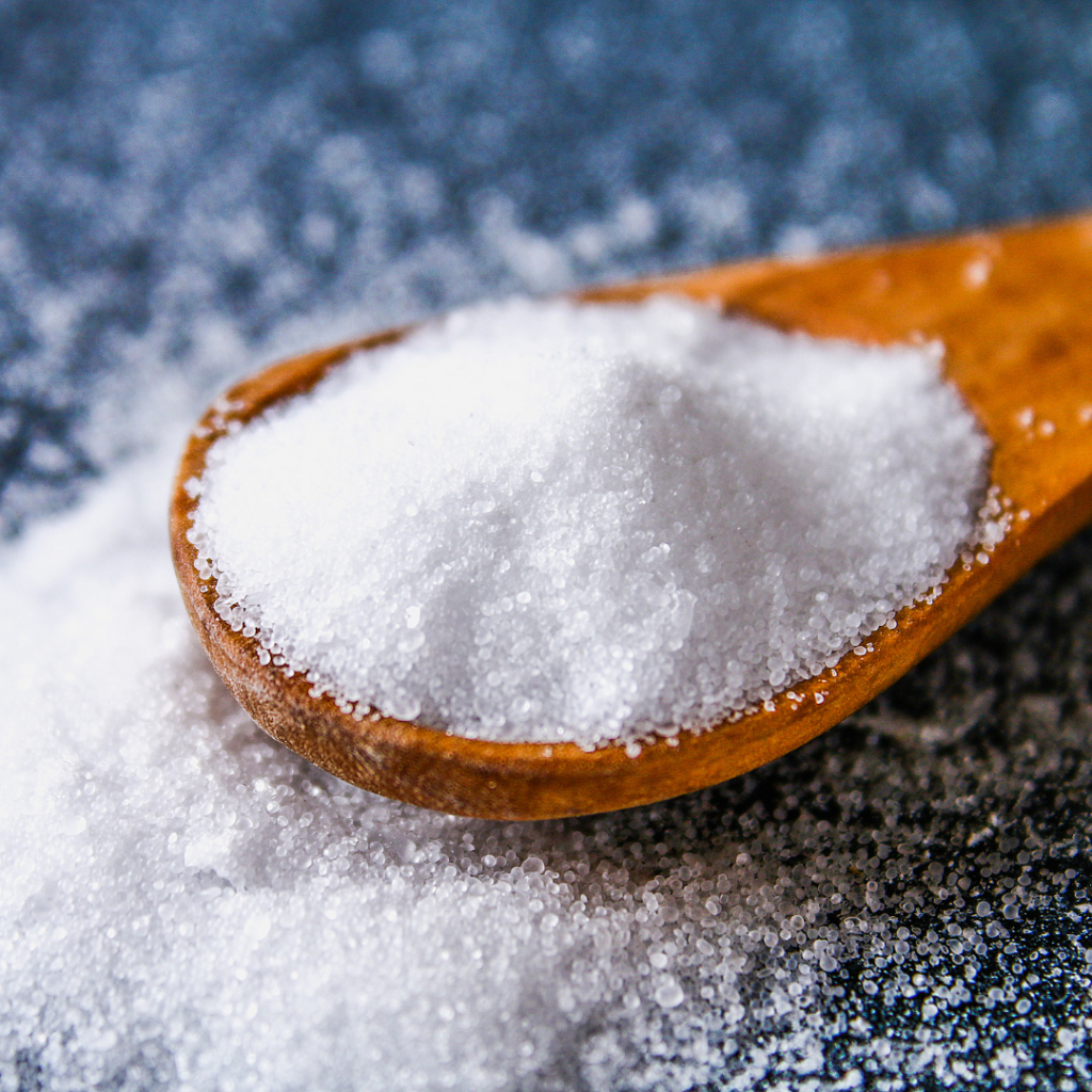 Table salt in a wooden spoon and spilled around it.