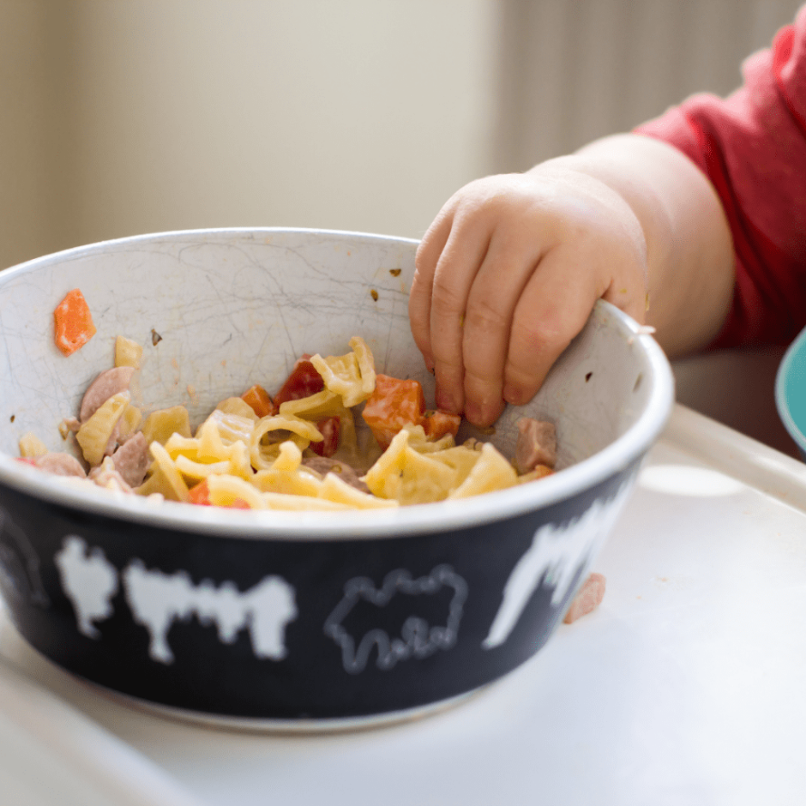 Baby grasping a bowl of pasta, showing babies can eat the same foods as parents do.