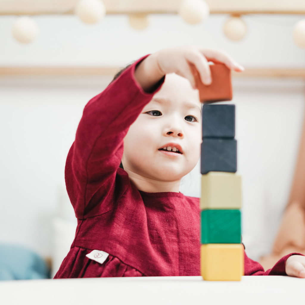 A toddler builds a block tower with wooden blocks of different colors.