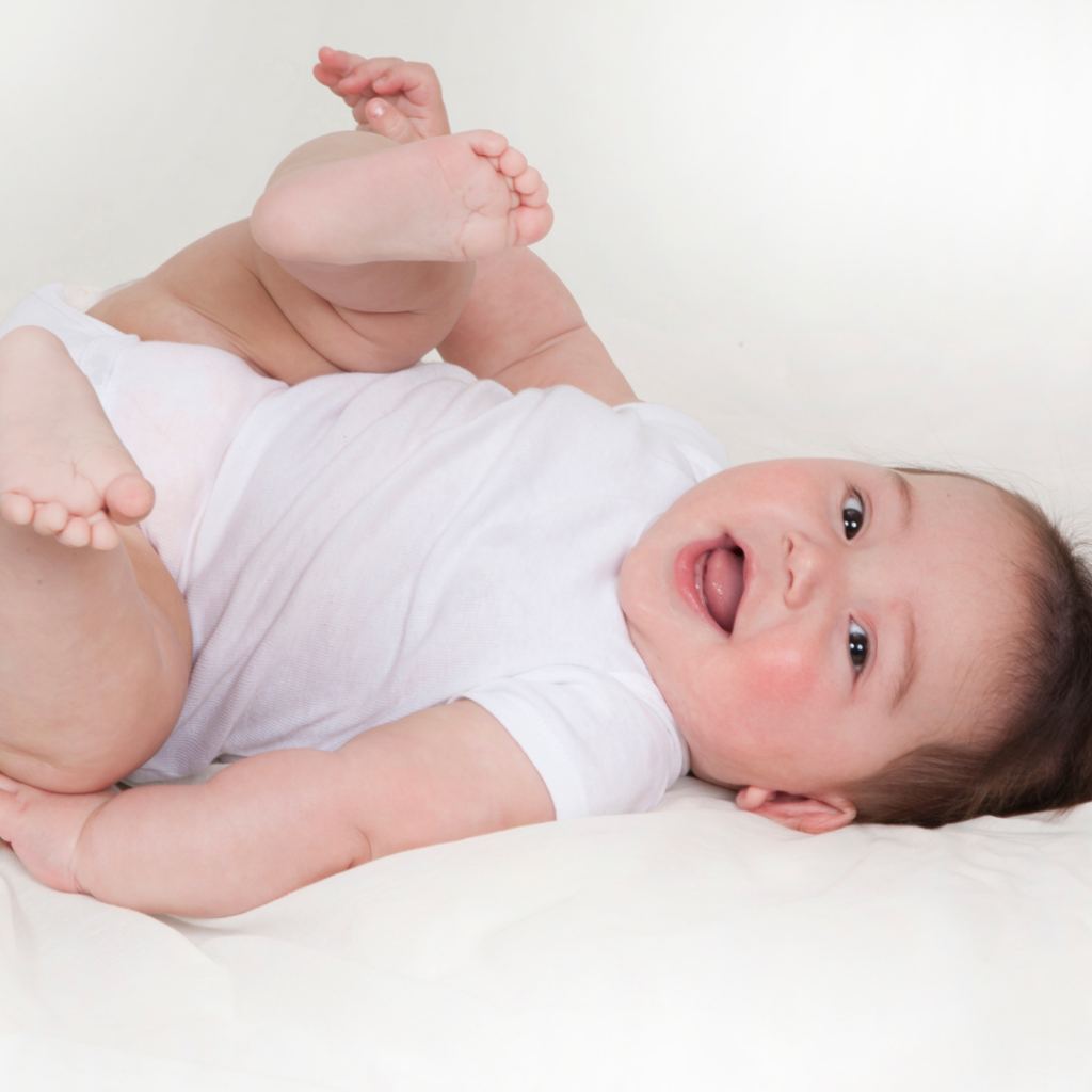 A baby in a white onesie smiles while lying down.