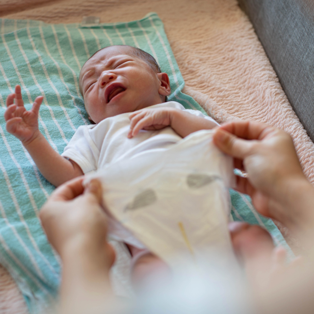 A newborn baby cries at the end of a diaper change while their parent closes the clean diaper.