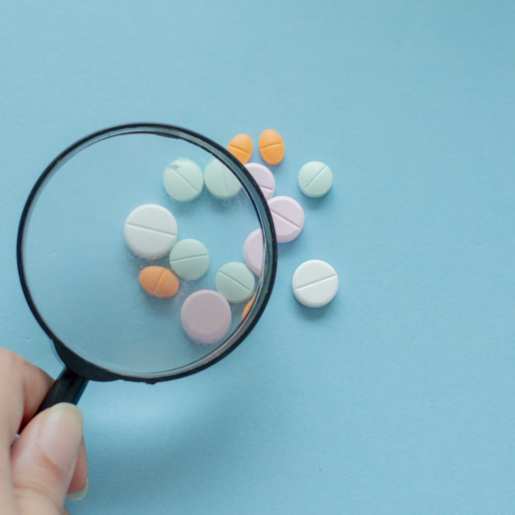 Colored pills being looked at under a magnifying glass.