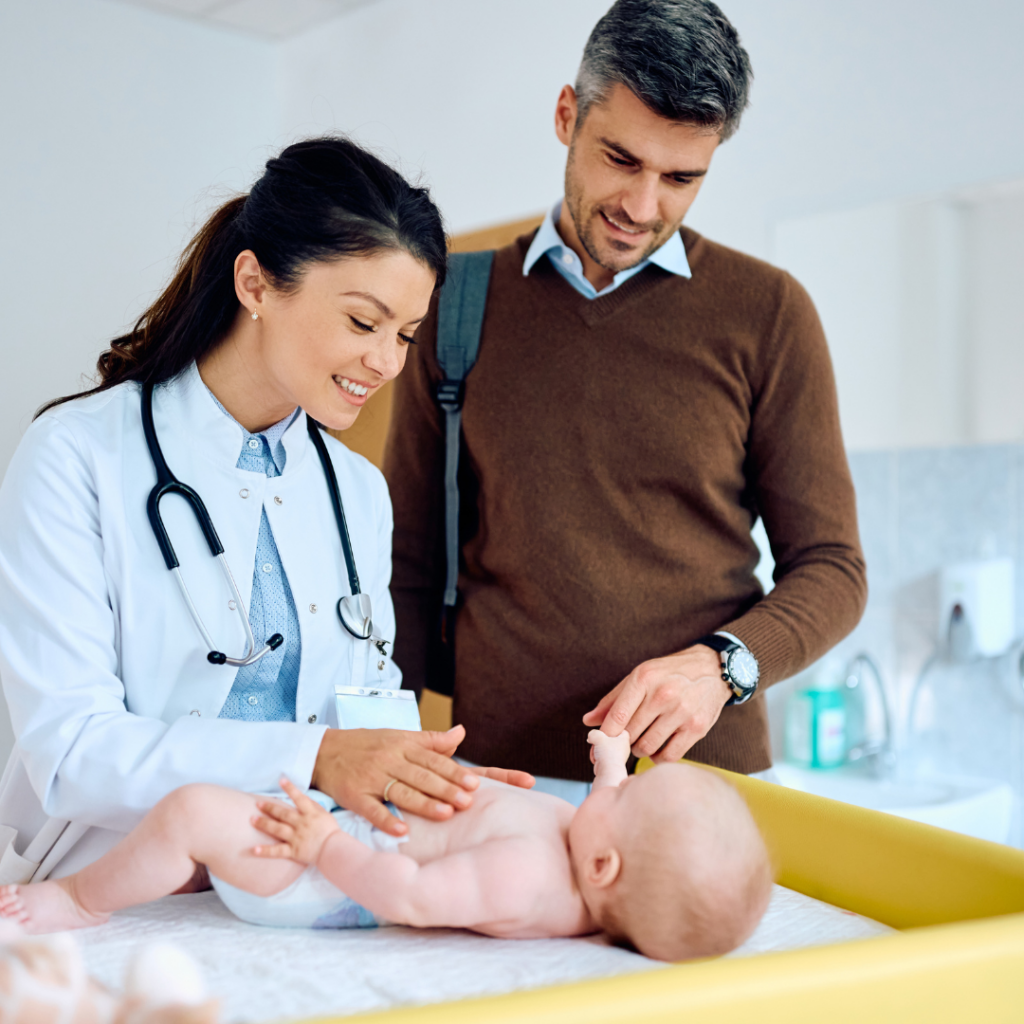 A doctor examines a baby's tummy while a parents stands by holding their hand.