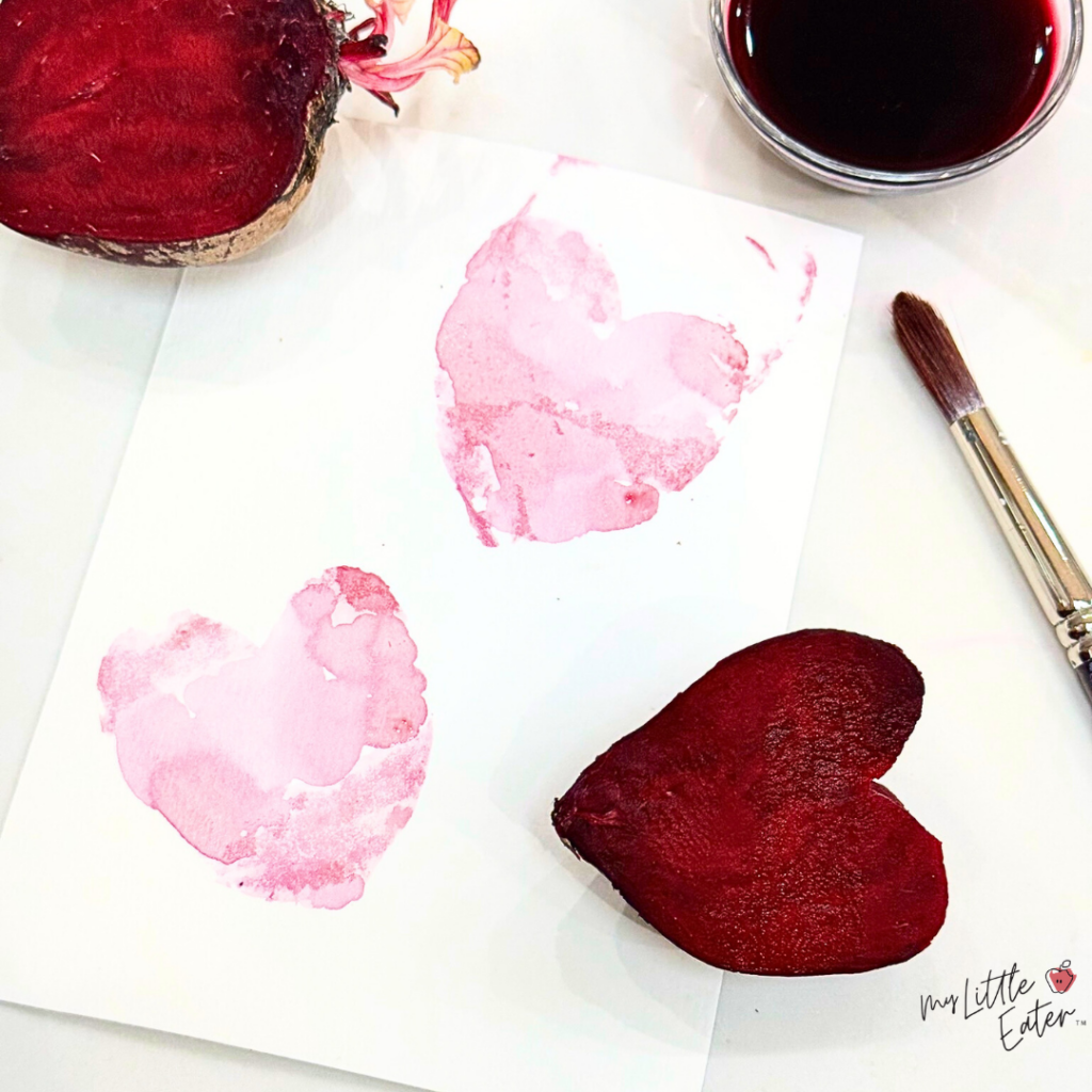 A beet cut into the shape of a heart and used as a stamp on paper to make red heart shapes.