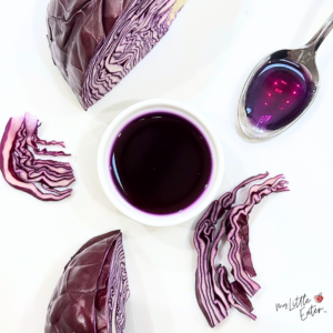 Purple natural food coloring made with purple cabbage, some liquid in a bowl and spoon with cabbage pieces around it.