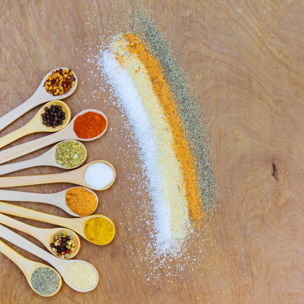 Spices of various colors in spoons laid out in a row.