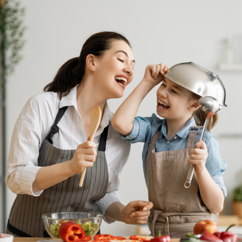 Mother and child cooking in the kitchen while acting silly and laughing together.