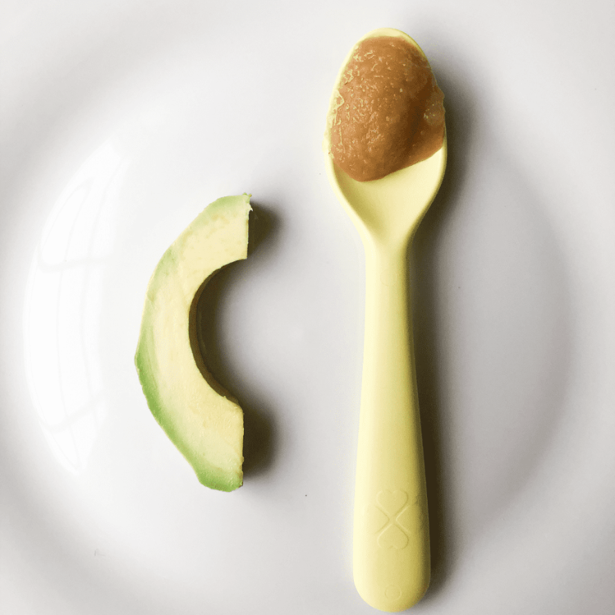 How to prepare food for baby, shown on a plate including a slice of avocado and applesauce on a spoon as new foods to try.