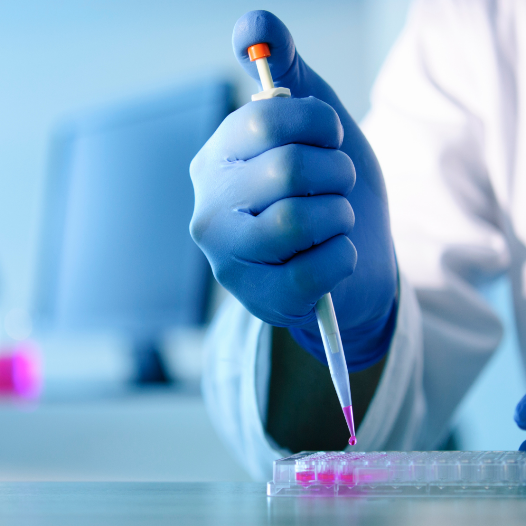 Scientist wearing a rubber glove and using a pipette to dispense liquid into small testing samples.