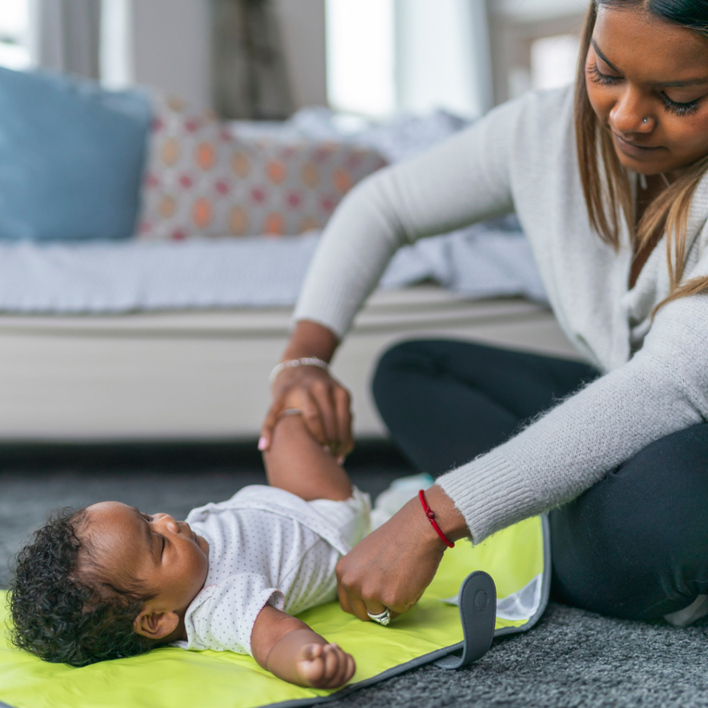 A mom gets ready to change a diaper on a change pad on the floor.