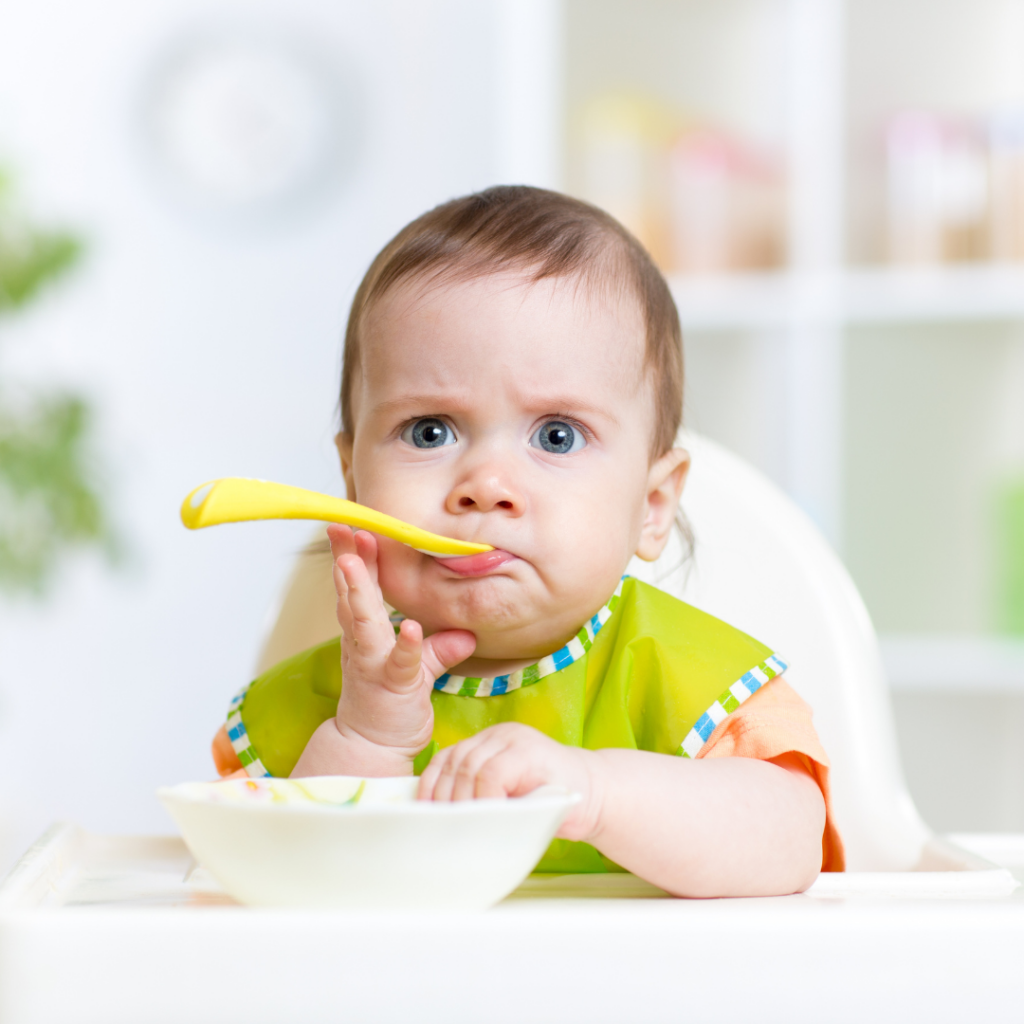 Baby eating in a high chair with a spoon in their mouth.