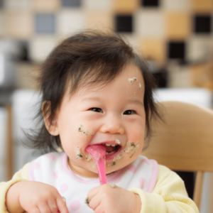 Baby sitting in their high chair eating healthy foods with their spoon.