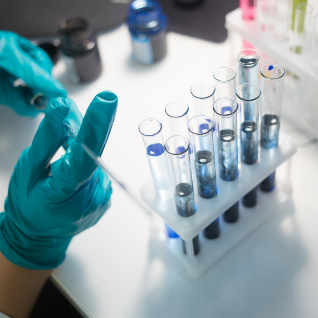 A scientist holding a pipette in front of test tubes while wearing rubber gloves.