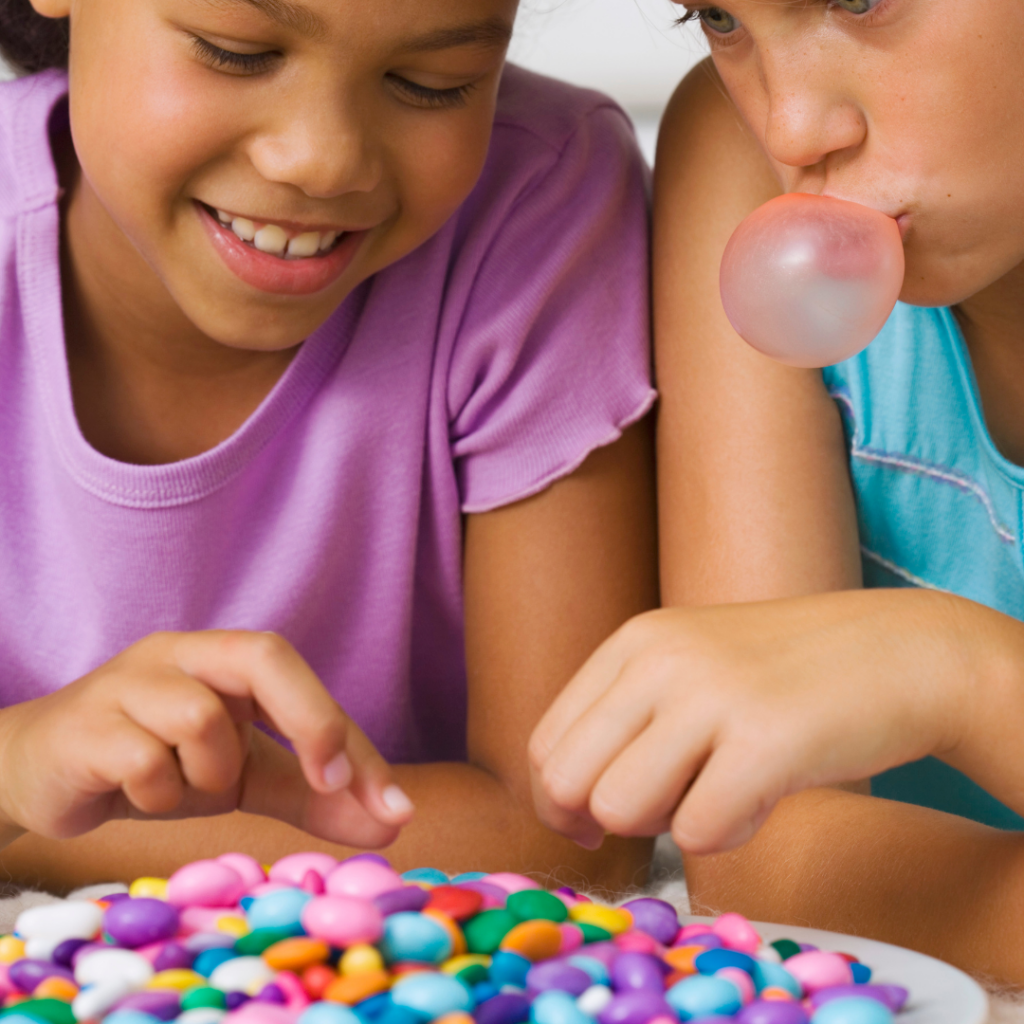 Two children looking at a bowl of colorful candy and choosing a piece each.