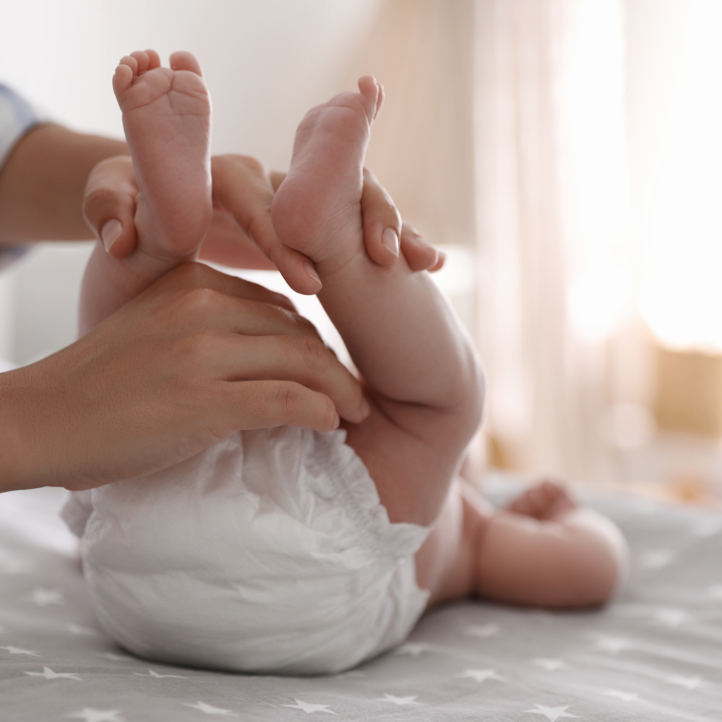 A parent holds their baby's legs before starting a diaper change for a bowel movement.