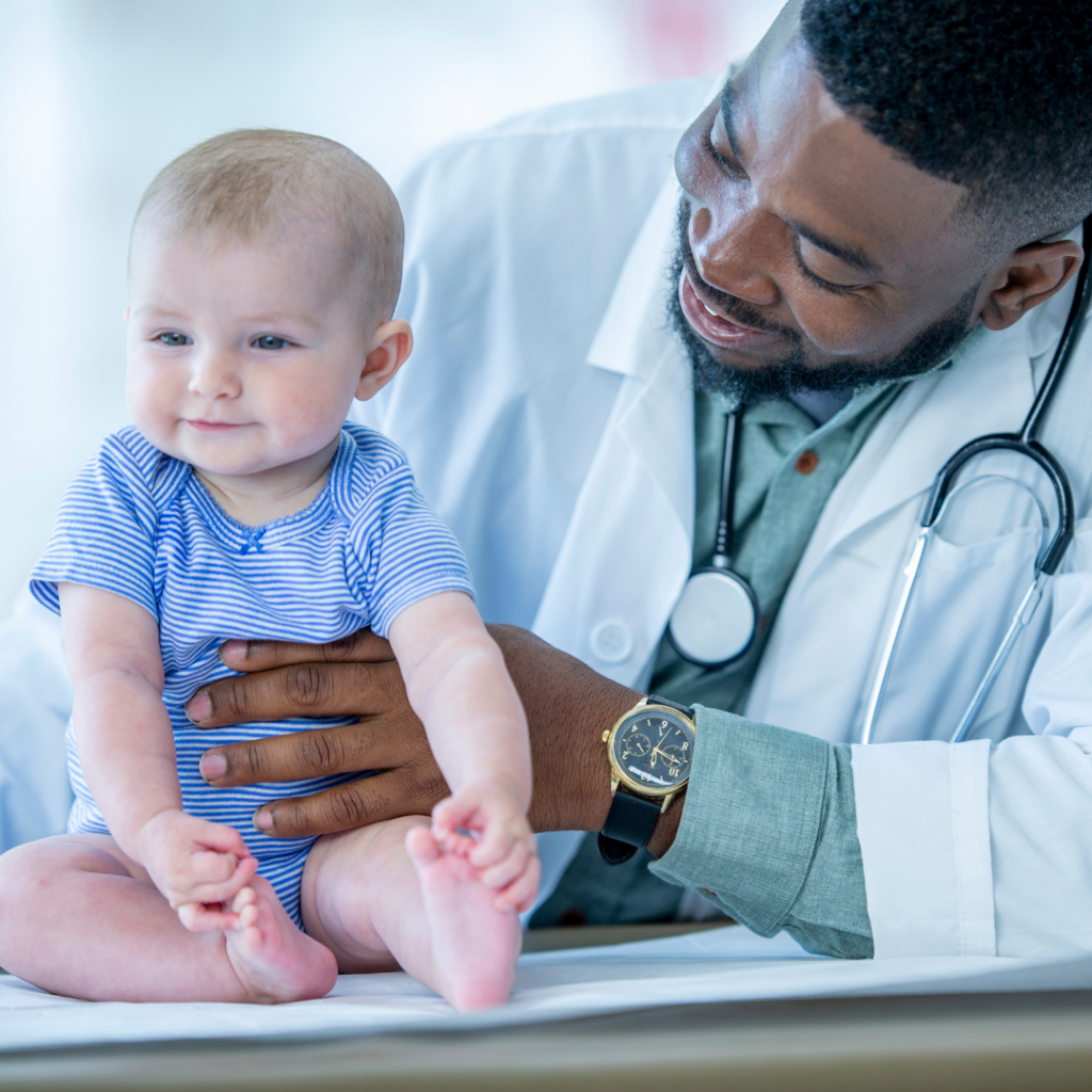 A baby sits on an exam table with their doctor beside them during a check up.