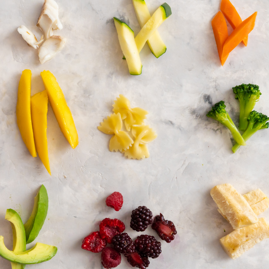 Various baby finger foods including avocado, berries, pasta, broccoli, chicken, banana, zucchinni, peppers, and carrots.