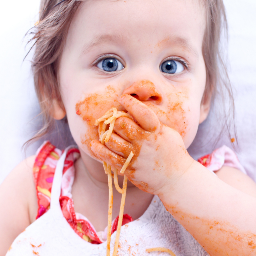 Baby using their palmar grasp to eat messy spaghetti noodles.