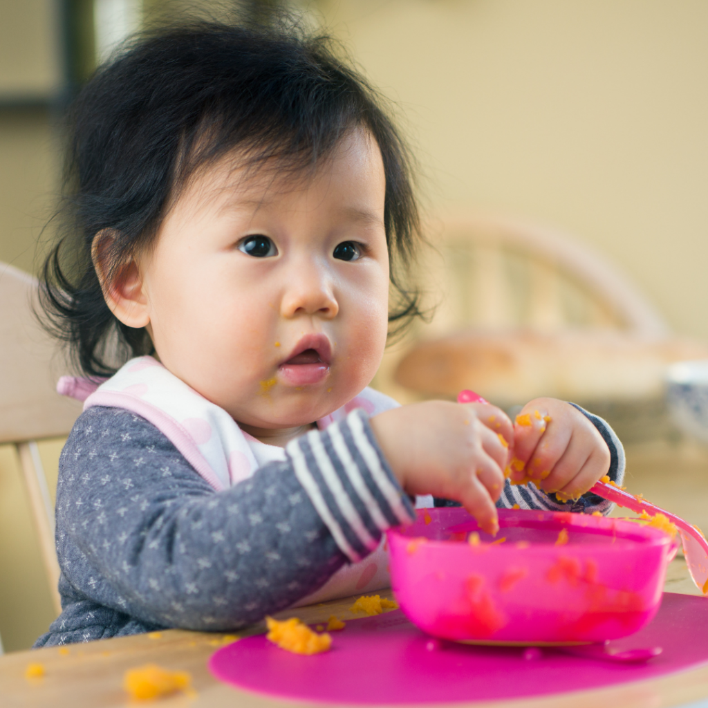 Infant in a high chair eating homemade sweet potato puree.