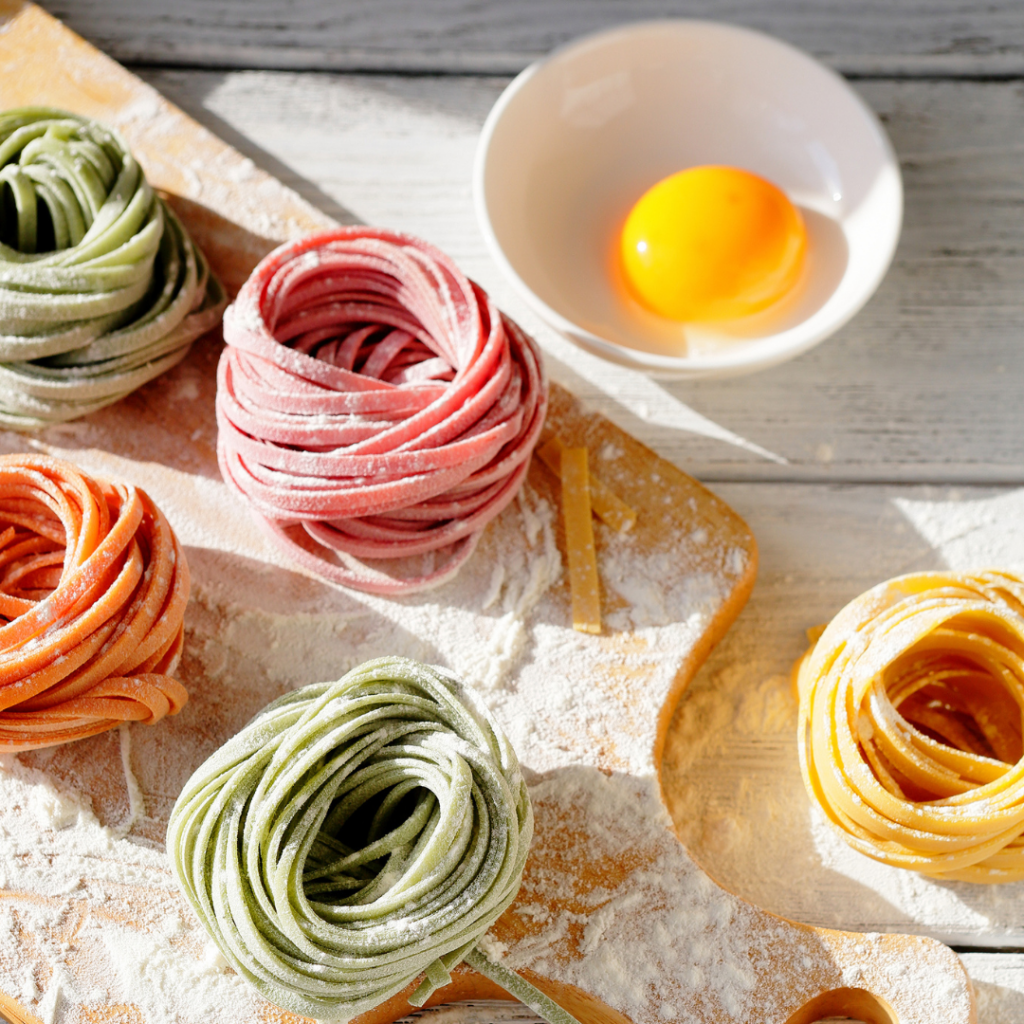 Homemade pasta for babies on a cutting board with a bowl containing one egg beside it.