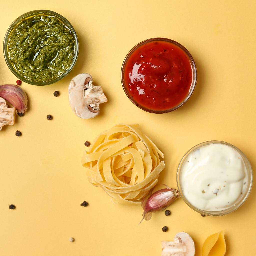 Pasta for baby rolled into a ball, surround by 3 sauce options: pesto, marinara, and alfredo sauce.