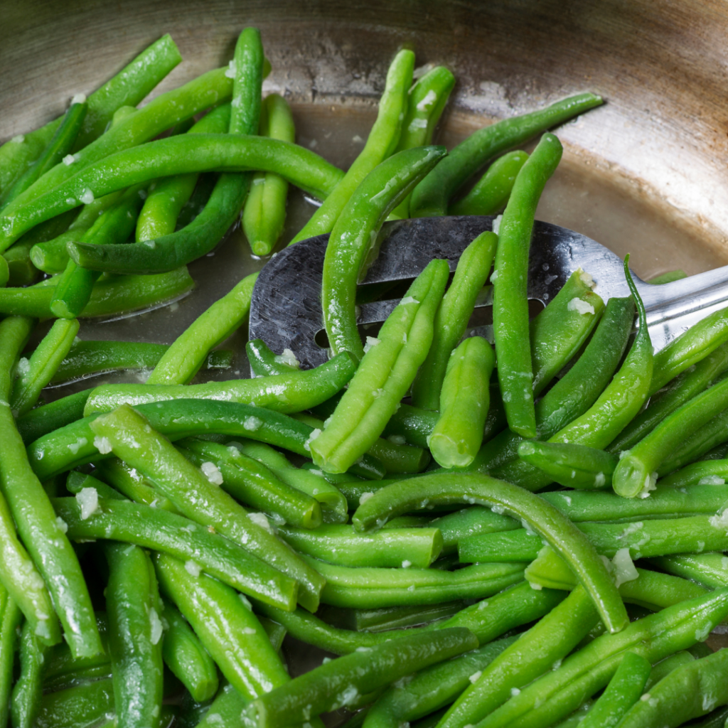 Green beans being sautéd with what looks like oil, garlic powder, and salt in a pan on medium heat or high heat.