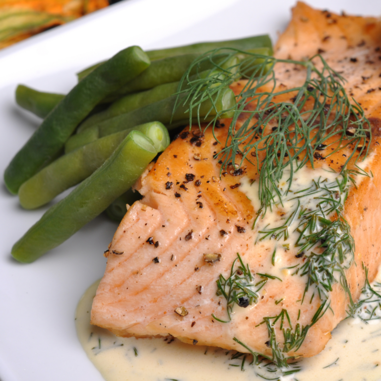 A plated meal of salmon with dill and lemon juice and steamed or roasted green beans on the side.