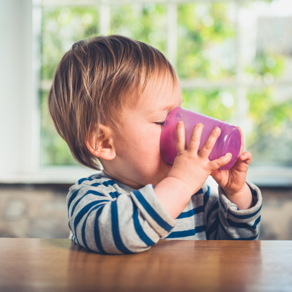 A toddler drinks from a purple, plastic open cup.