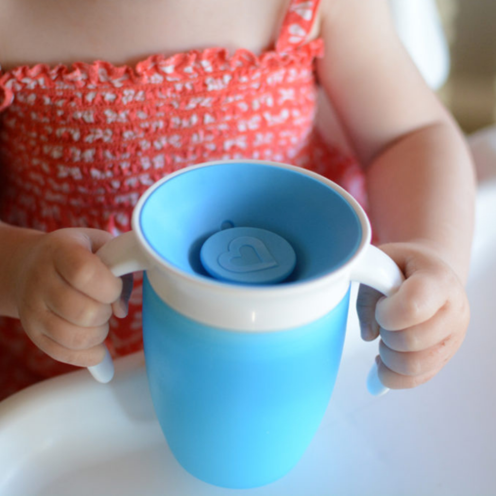 Toddler holding both handles of a blue Munchkin 360 cup.